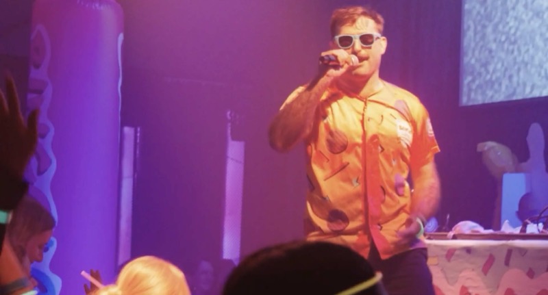 Scott Rowan in sunglasses performing into a microphone at a Bingo Loco show