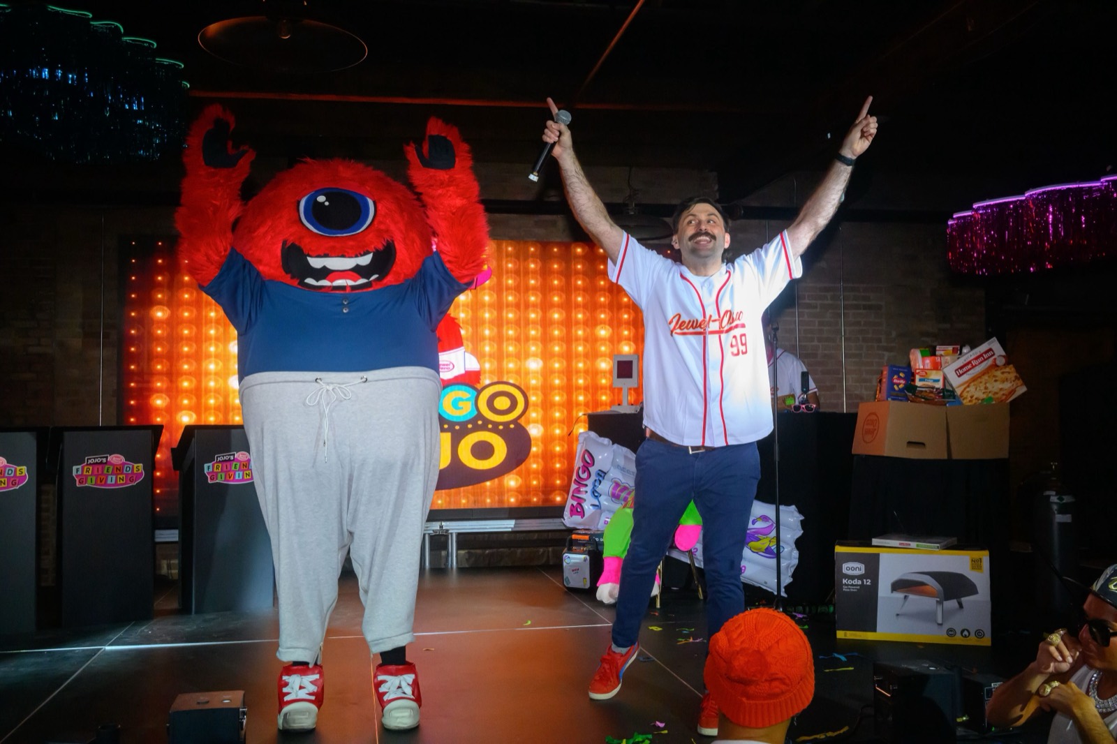 Scott Rowan on stage with a microphone, arms raised, next to the Bingo Loco mascot